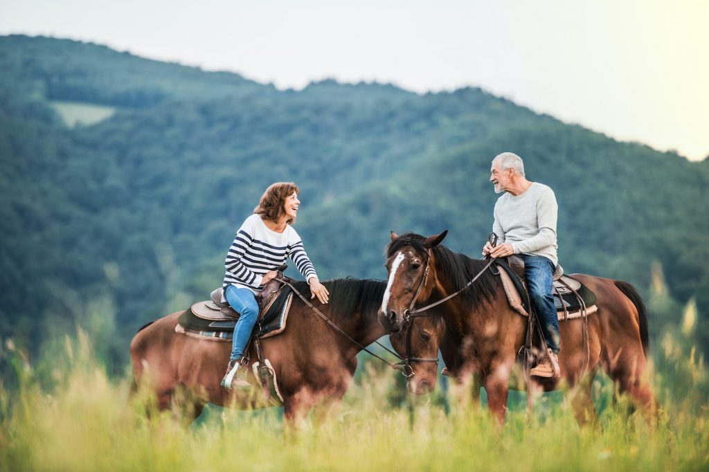 A senior couple riding horses in nature.