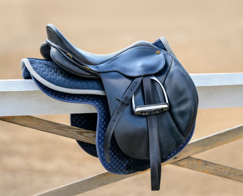 Black English saddle hanging on fence near stables.